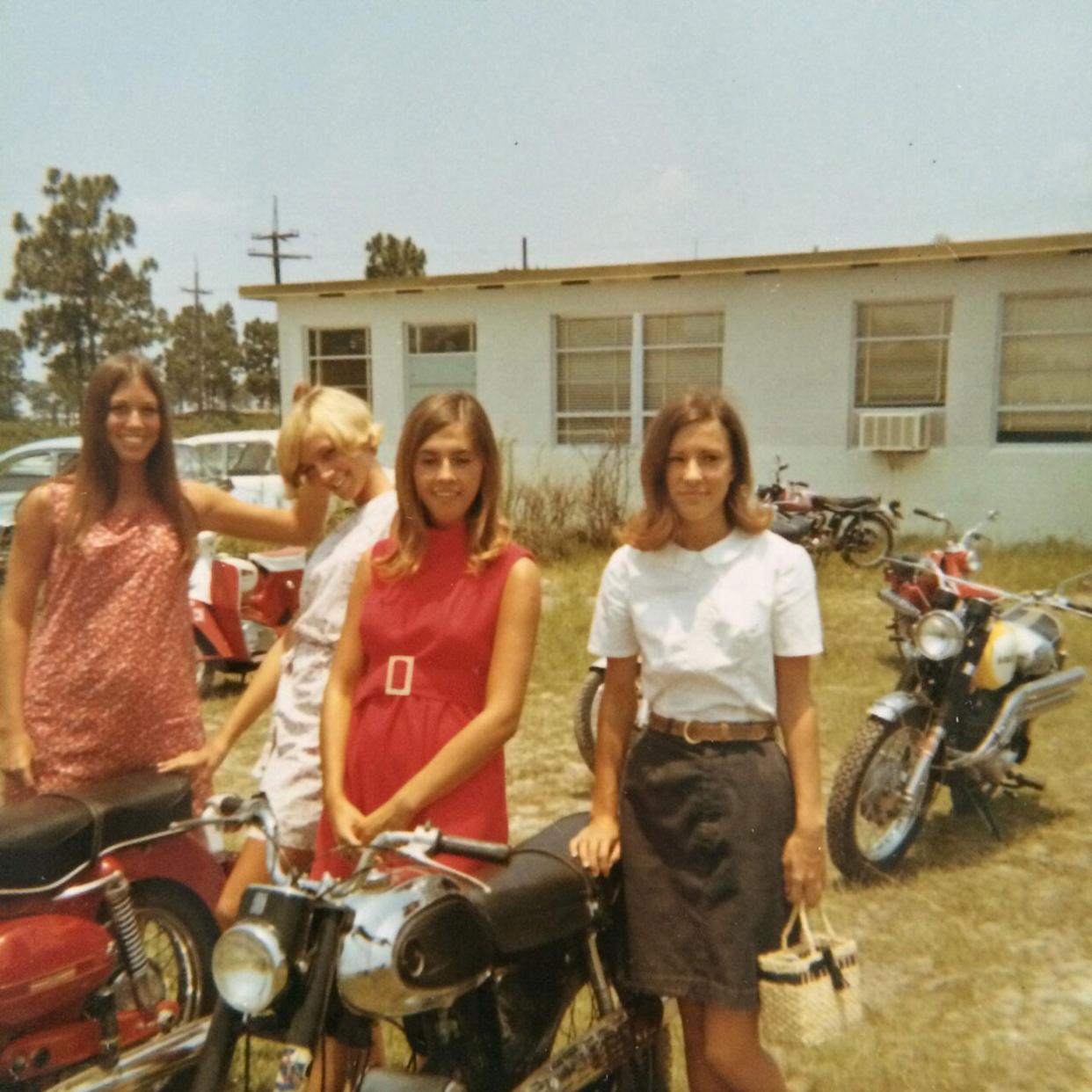 A group of young women smiling and standing around their motorcycles