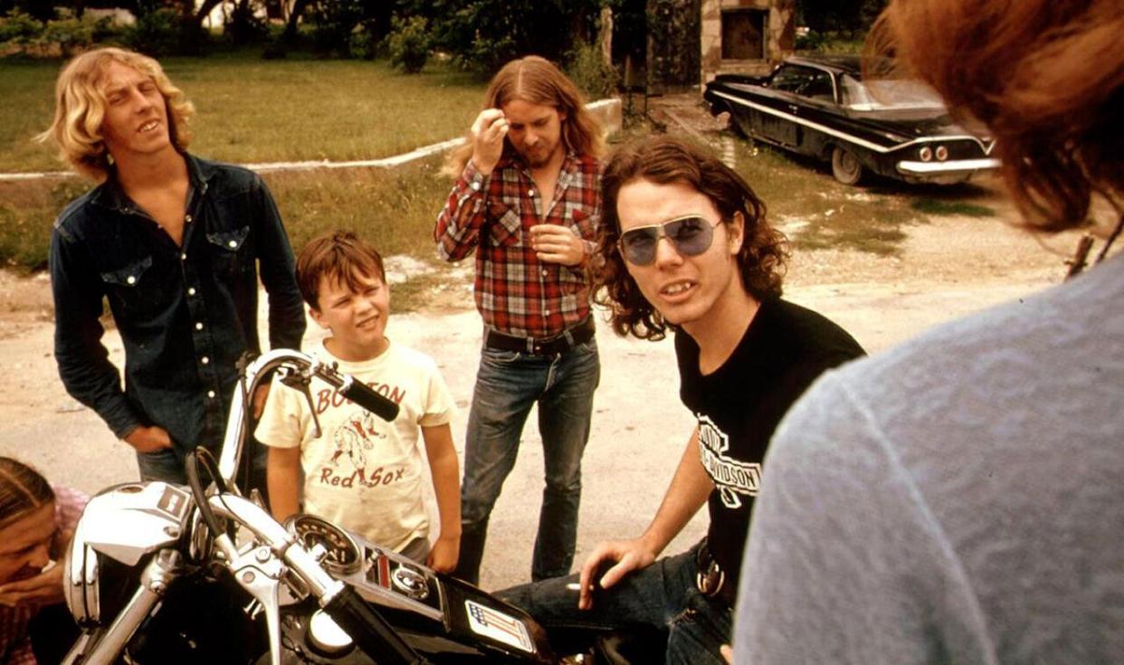Friends standing around a guy on a motorcycle