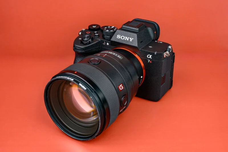 A Sony α7R mirrorless camera with a large lens displayed on an orange background.
