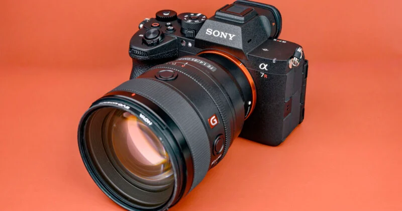 A Sony Alpha 7R mirrorless camera with a large zoom lens attached, placed on an orange surface.